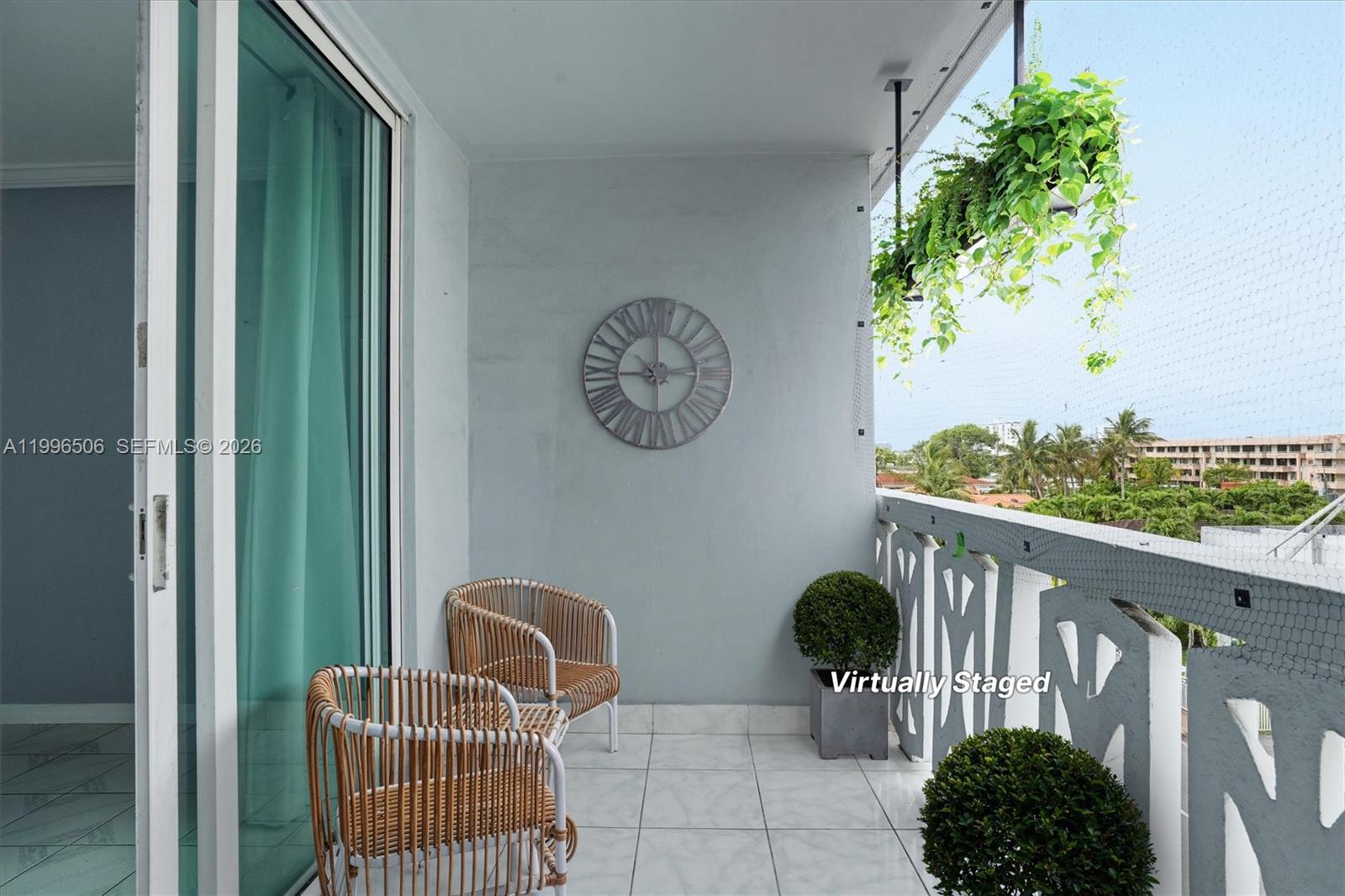 A balcony features two rattan chairs, a wall clock, potted plants, and a white railing — 8233 Harding Ave # 504, Miami Beach FL 33141, MIAMI BEACH, FL