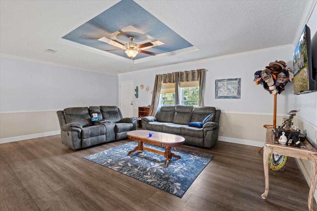 A living room features gray sofas, a blue-accented tray ceiling, and wood-look flooring — 87 NE 544TH STREET, OLD TOWN, FL
