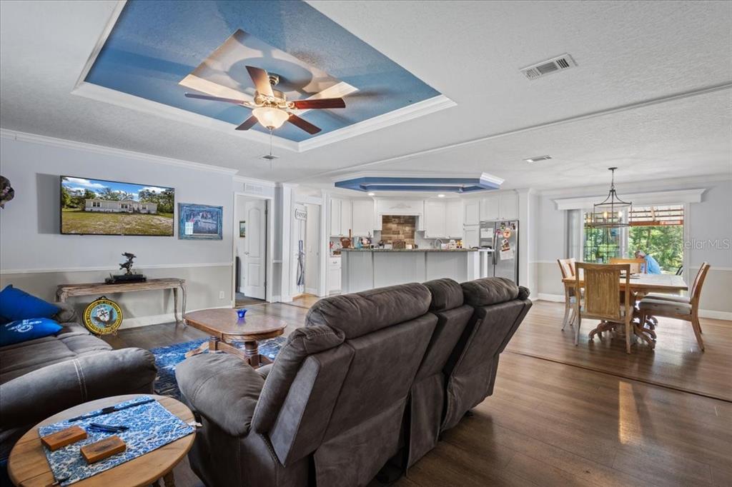 An open-concept living room and kitchen featuring a blue tray ceiling and wood flooring — 87 NE 544TH STREET, OLD TOWN, FL