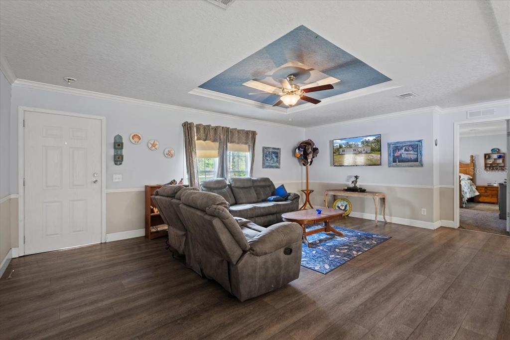 A living room features wood-look flooring, a blue tray ceiling, and a gray sectional sofa — 87 NE 544TH STREET, OLD TOWN, FL