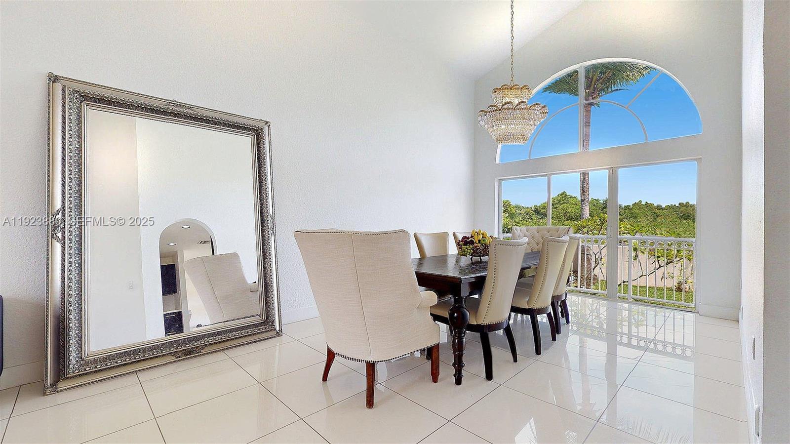 A dining room features a large mirror, a crystal chandelier, and a tall arched window — 14633 SW 132nd Ave, Miami FL 33186, MIAMI, FL