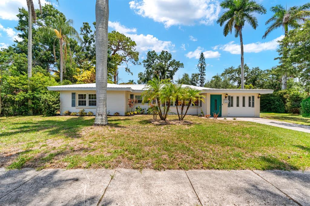 A single-story house with light siding, a teal front door, and palm trees in the yard — 2415 2ND AVENUE E, BRADENTON, FL