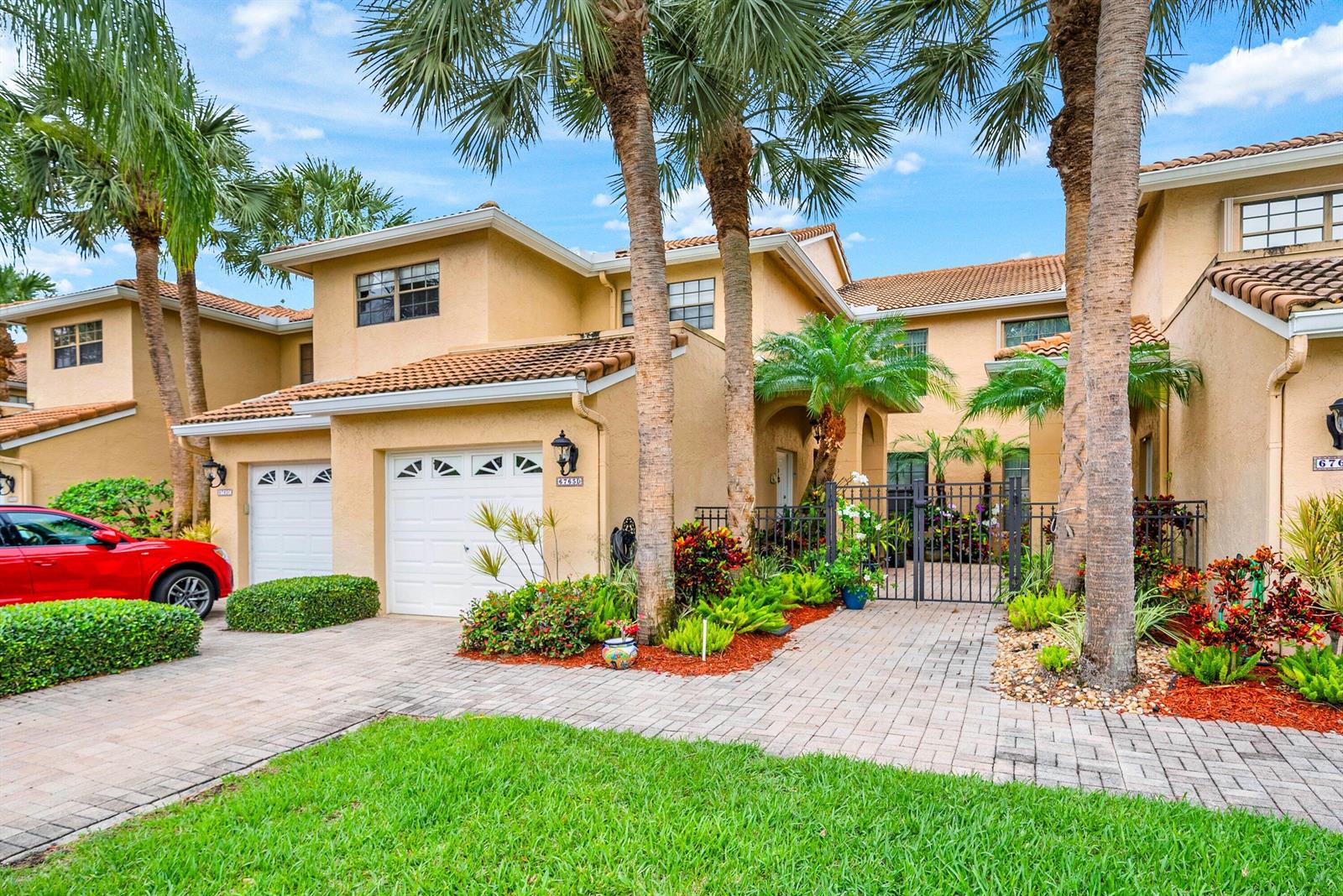 A two-story tan stucco townhouse features a paved driveway, a garage, and palm trees — 6765 Montego Bay Boulevard # D, Boca Raton FL 33433, BOCA RATON, FL