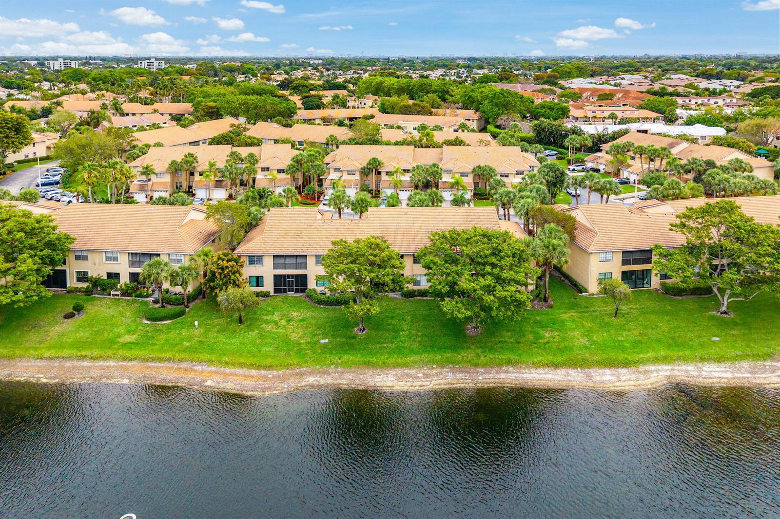 An aerial view shows multi-unit townhomes with tan roofs situated along a lakefront lawn — 6765 Montego Bay Boulevard # D, Boca Raton FL 33433, BOCA RATON, FL