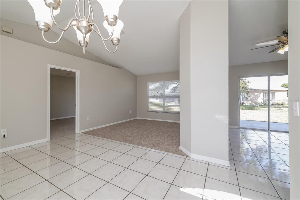 A dining area with tile flooring transitions into a carpeted living space with a chandelier — 188 ANZIO DRIVE, KISSIMMEE, FL
