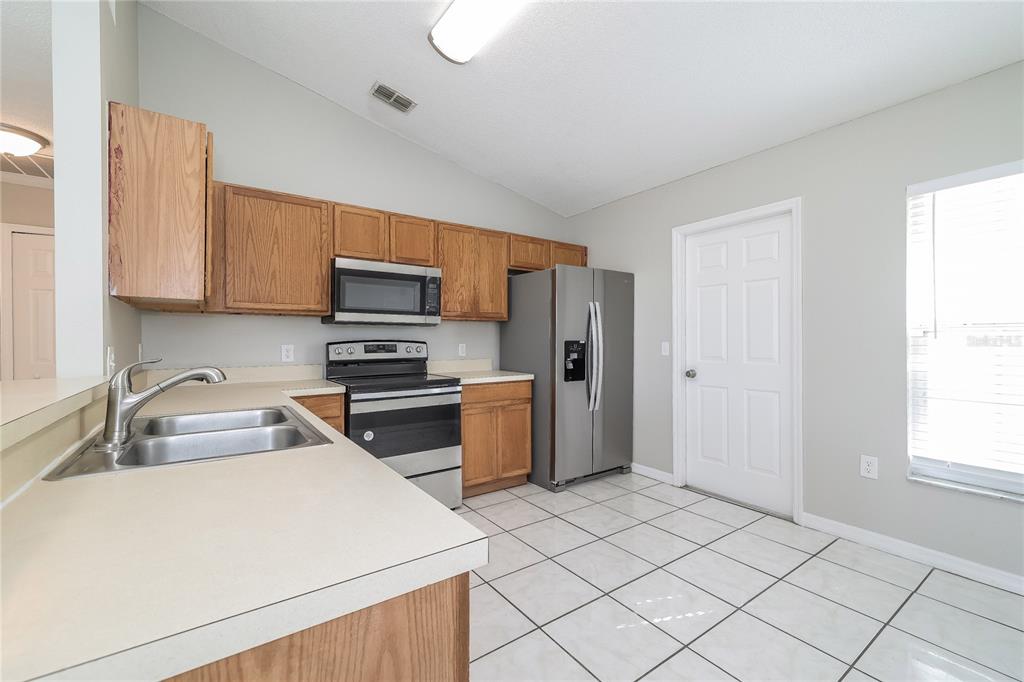 A kitchen features light-colored countertops, wooden cabinets, stainless steel appliances, and white tiled flooring — 188 ANZIO DRIVE, KISSIMMEE, FL