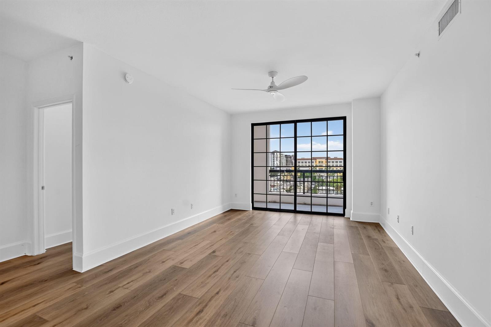 An empty room with white walls, wood-look flooring, a ceiling fan, and black-framed sliding doors — 233 S Federal Highway # 623, Boca Raton FL 33432, BOCA RATON, FL