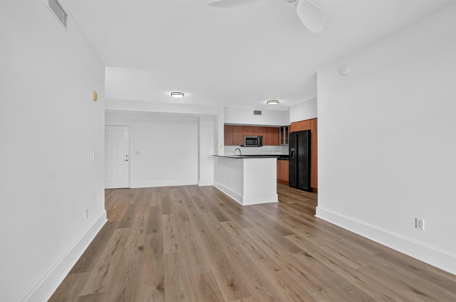 An open-concept living area features light wood-look flooring, white walls, and a kitchen with wood cabinets — 233 S Federal Highway # 623, Boca Raton FL 33432, BOCA RATON, FL