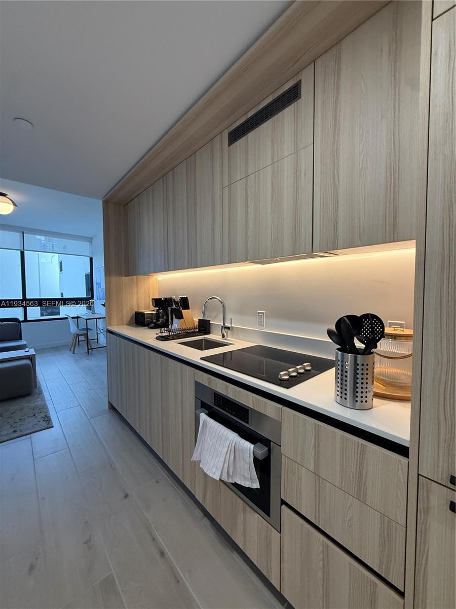 A modern kitchen features light wood cabinetry, white countertops, and integrated appliances — 225 N Miami ave # 501, Miami FL 33128, MIAMI, FL