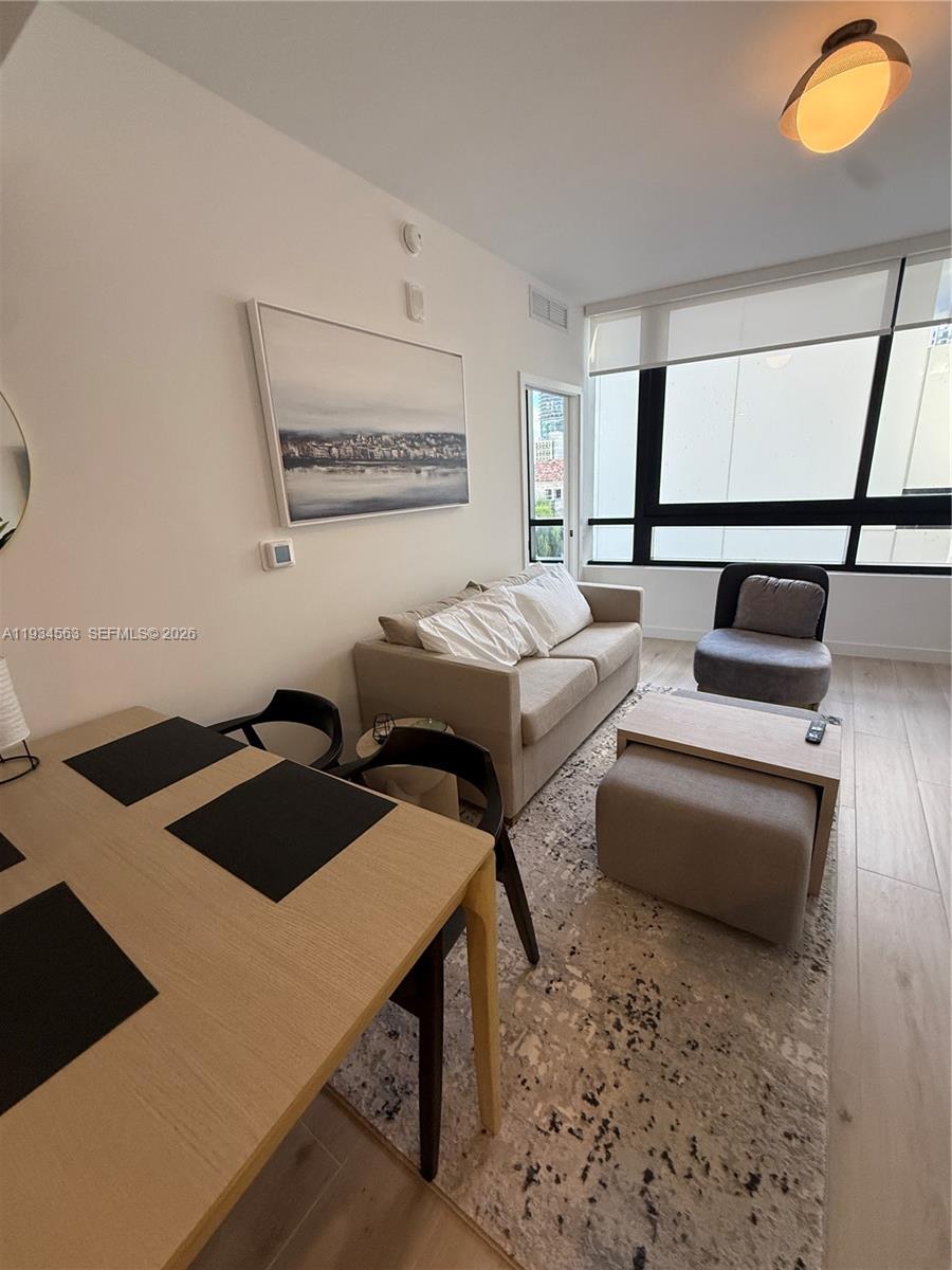 A living and dining area features light wood flooring, a beige sofa, and large windows — 225 N Miami ave # 501, Miami FL 33128, MIAMI, FL