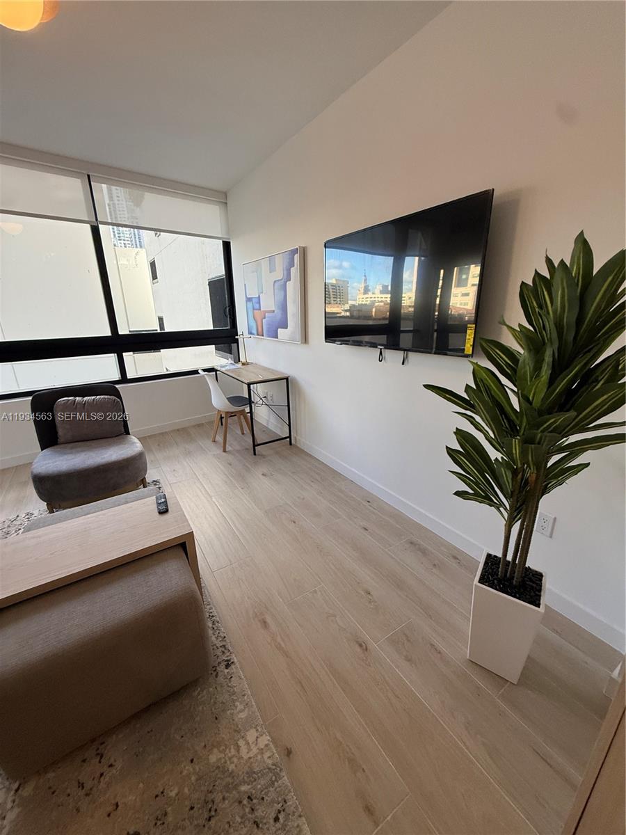A modern living room features light wood flooring, a wall-mounted television, and a small desk — 225 N Miami ave # 501, Miami FL 33128, MIAMI, FL