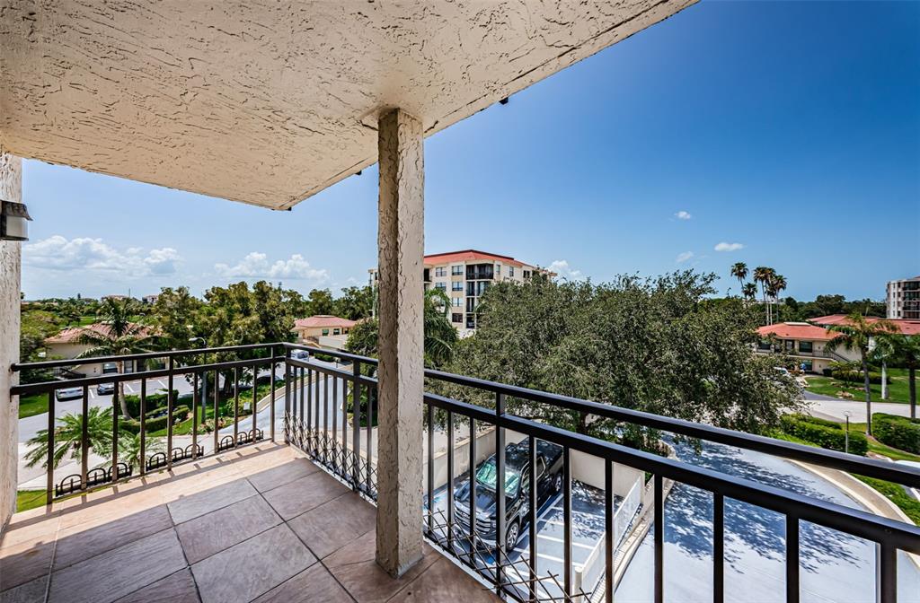 A tiled balcony with a metal railing overlooks a parking area, trees, and nearby buildings — 6177 SUN BOULEVARD UNIT 404, ST PETERSBURG, FL