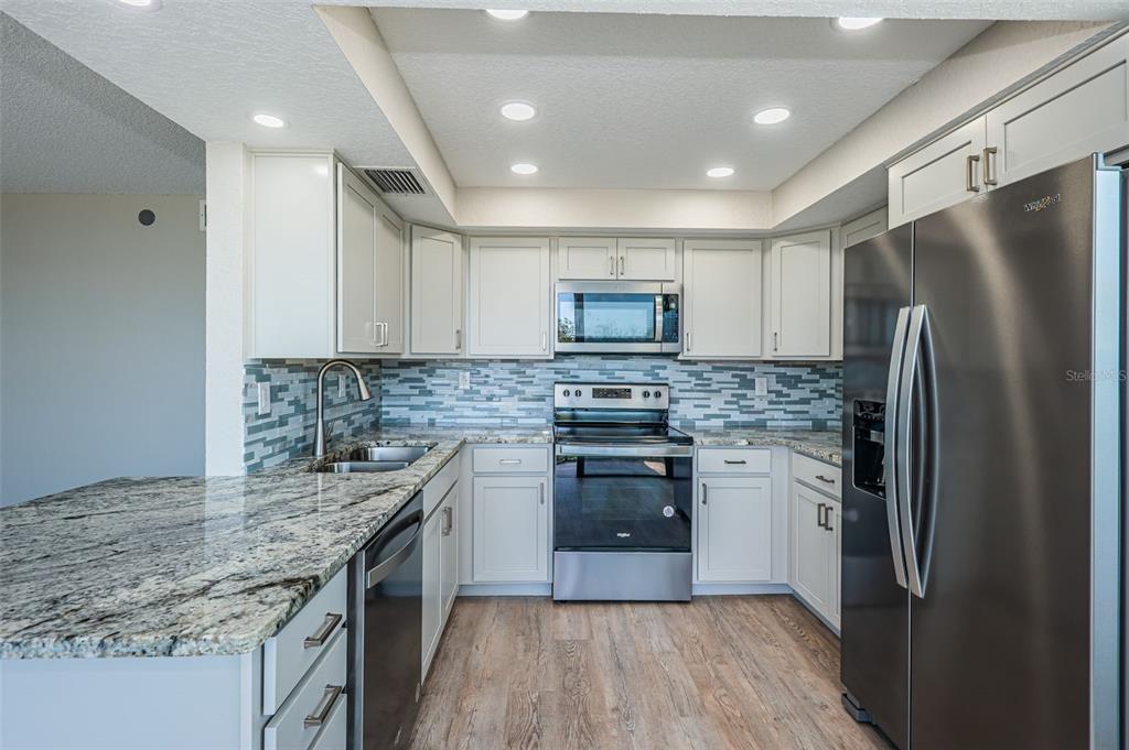 A kitchen features white cabinets, granite countertops, a tiled backsplash, and stainless steel appliances — 6177 SUN BOULEVARD UNIT 404, ST PETERSBURG, FL