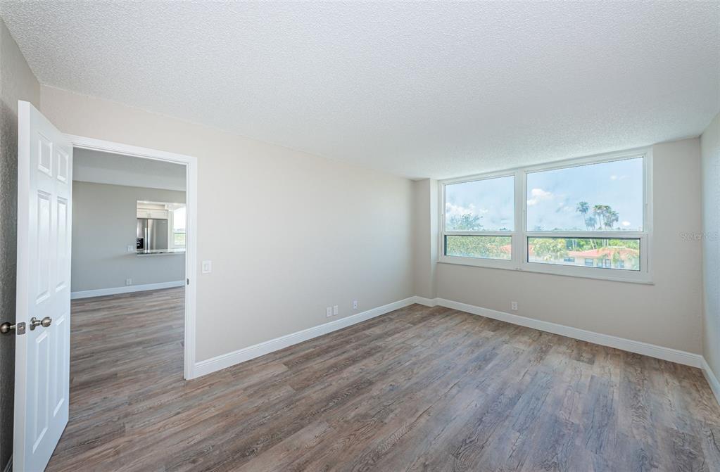 An empty room with wood-look flooring and a large window overlooking palm trees — 6177 SUN BOULEVARD UNIT 404, ST PETERSBURG, FL