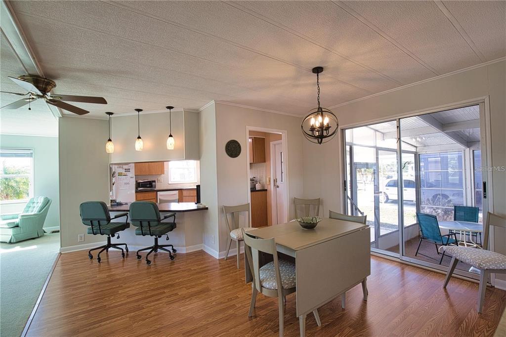 A dining area with wood-look flooring, a table, and a kitchen pass-through with bar stools — 402 CHIQUITA, NORTH PORT, FL