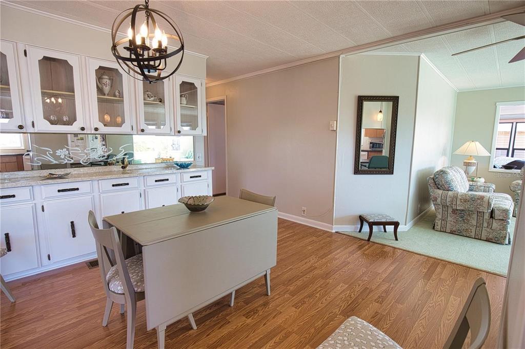 A dining area with white cabinets, a drop-leaf table, and a view into the living room — 402 CHIQUITA, NORTH PORT, FL
