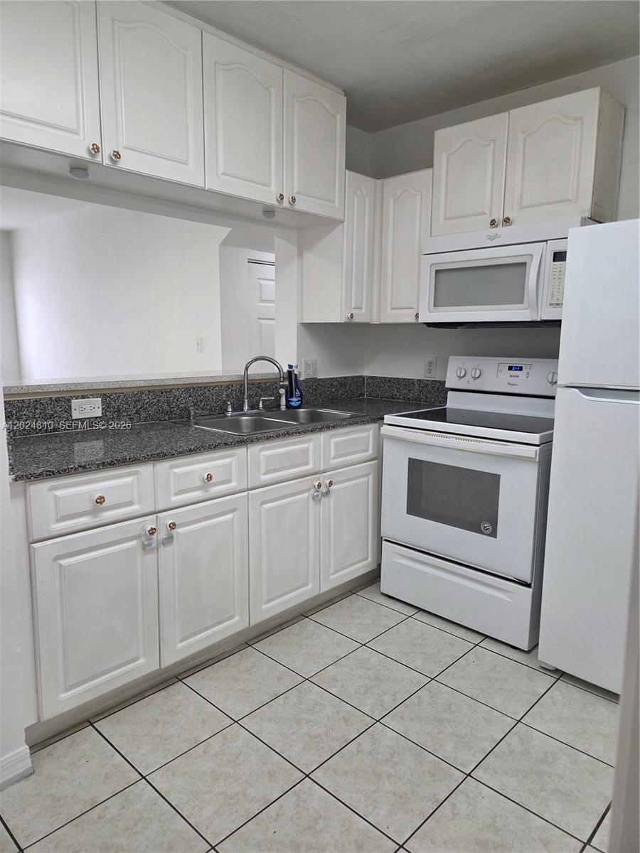A kitchen features white cabinets, granite countertops, white appliances, and light-colored tile flooring — MIAMI, FL