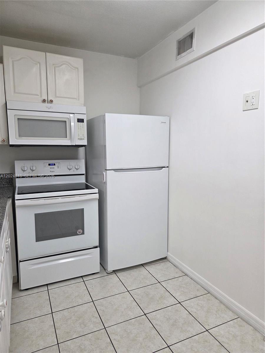 A kitchen features white appliances, white cabinets, and light-colored tiled flooring — MIAMI, FL