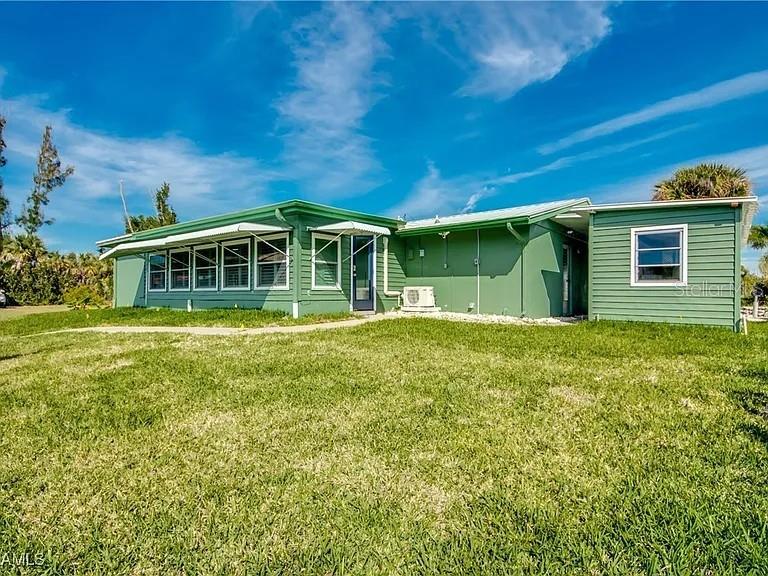 A green, single-story house with horizontal siding stands on a grassy lawn under blue skies — 2891 CUSSELL DRIVE, ST JAMES CITY, FL