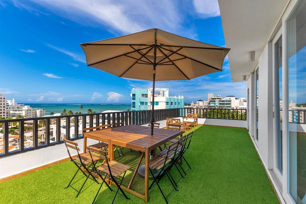 A balcony with artificial turf, a wooden dining set with an umbrella, and ocean views — 7 CALLE ROSA UNIT PH, CAROLINA, PR