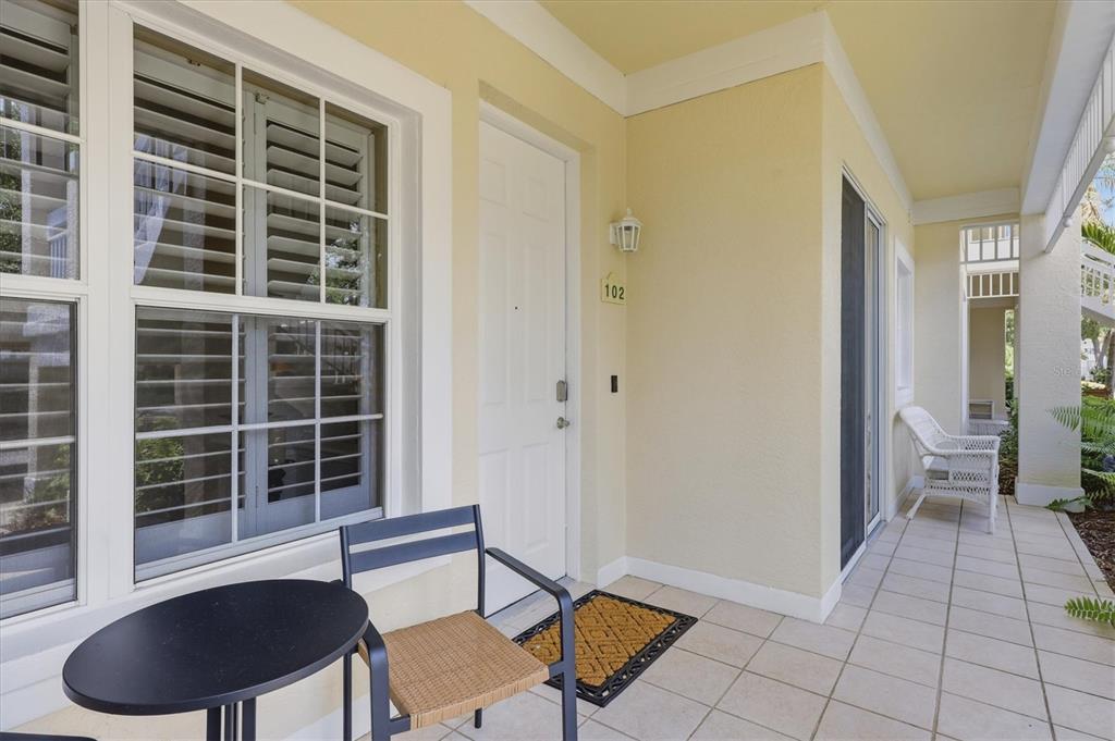 A covered patio features a white door labeled 102, tiled flooring, and outdoor furniture — 3510 54TH DRIVE W UNIT 102, BRADENTON, FL