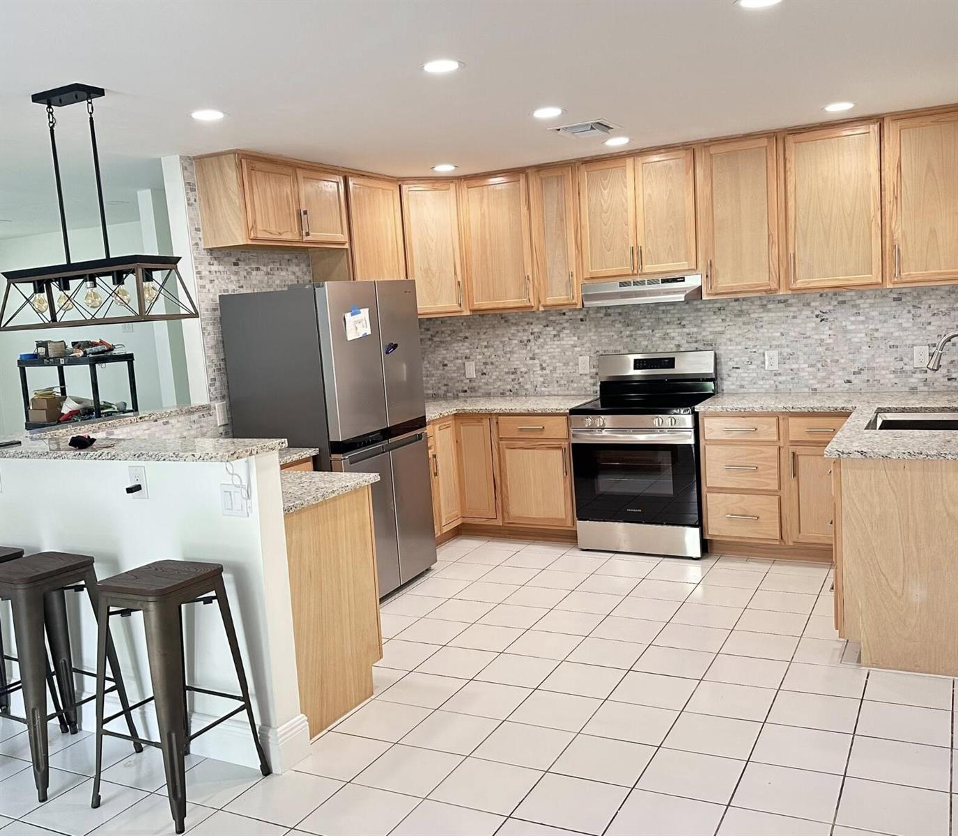 A kitchen features light wood cabinets, granite countertops, stainless steel appliances, and white tile flooring — 117 Yacht View Lane, FL 34946, FL