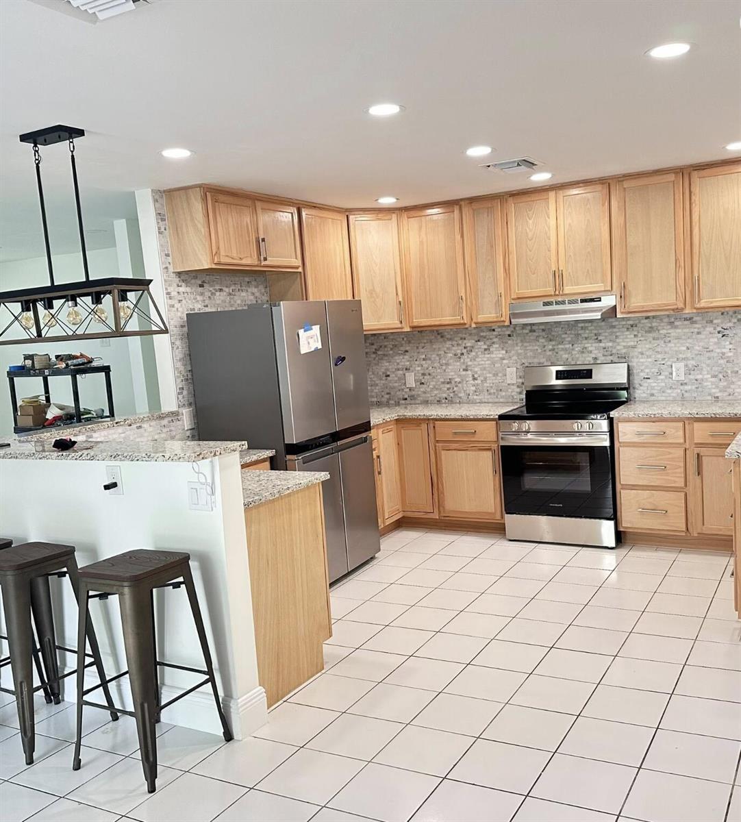 A kitchen features light wood cabinets, stainless steel appliances, granite countertops, and a tile floor — 117 Yacht View Lane, FL 34946, FL