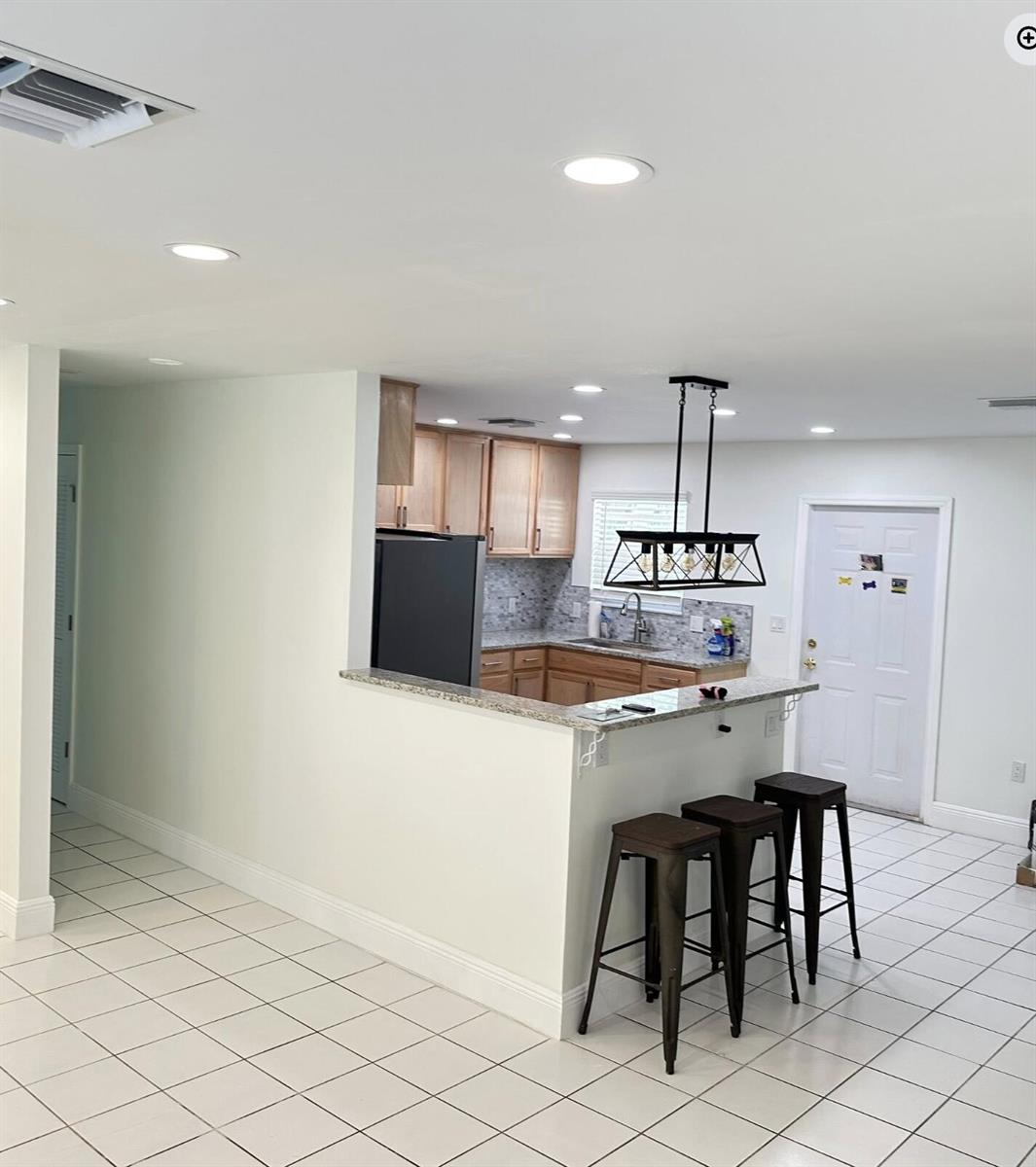 A kitchen with light wood cabinets, granite countertops, and a breakfast bar with three stools — 117 Yacht View Lane, FL 34946, FL