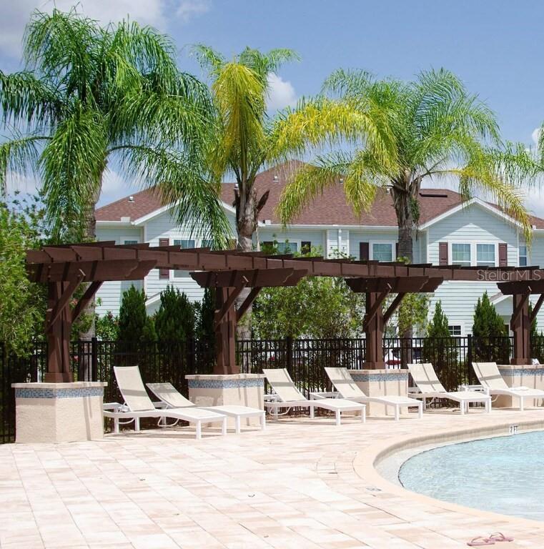 A swimming pool area features lounge chairs under a wooden pergola with palm trees nearby — 3211 WISH AVENUE, KISSIMMEE, FL