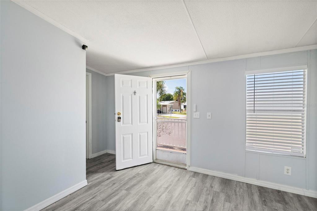 An interior room with light blue walls, gray wood-look flooring, and an open exterior door — 1000 KINGS HIGHWAY UNIT 101, PORT CHARLOTTE, FL
