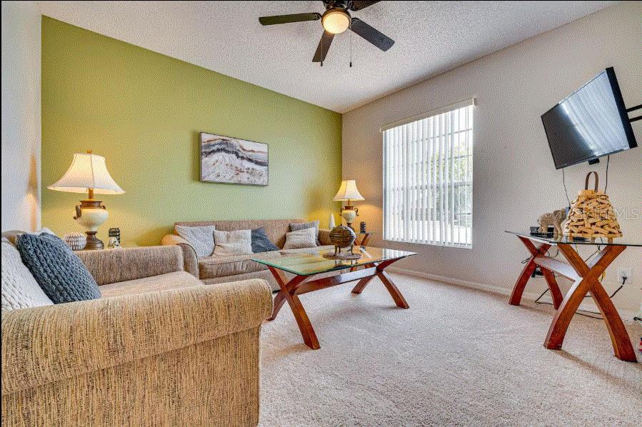 A living room features a green accent wall, beige carpet, a ceiling fan, and furniture — 136 SUNSET VIEW DRIVE, DAVENPORT, FL