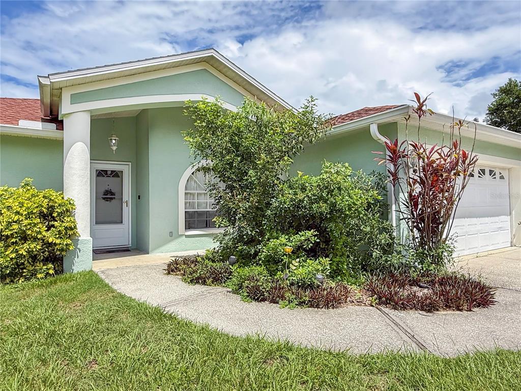 A light green house exterior features a white front door, arched window, and attached garage — 29708 69TH STREET N, CLEARWATER, FL