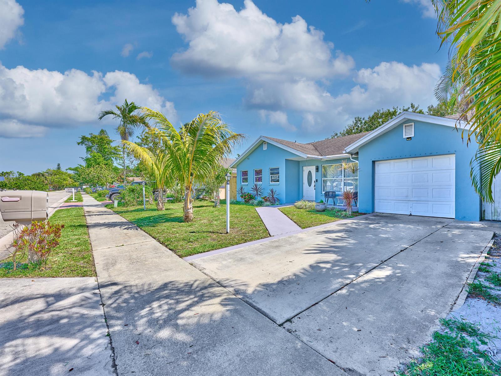 A light blue single-story house features a concrete driveway, a front lawn, and palm trees — 9020 SW 8th Street, Boca Raton FL 33433, BOCA RATON, FL