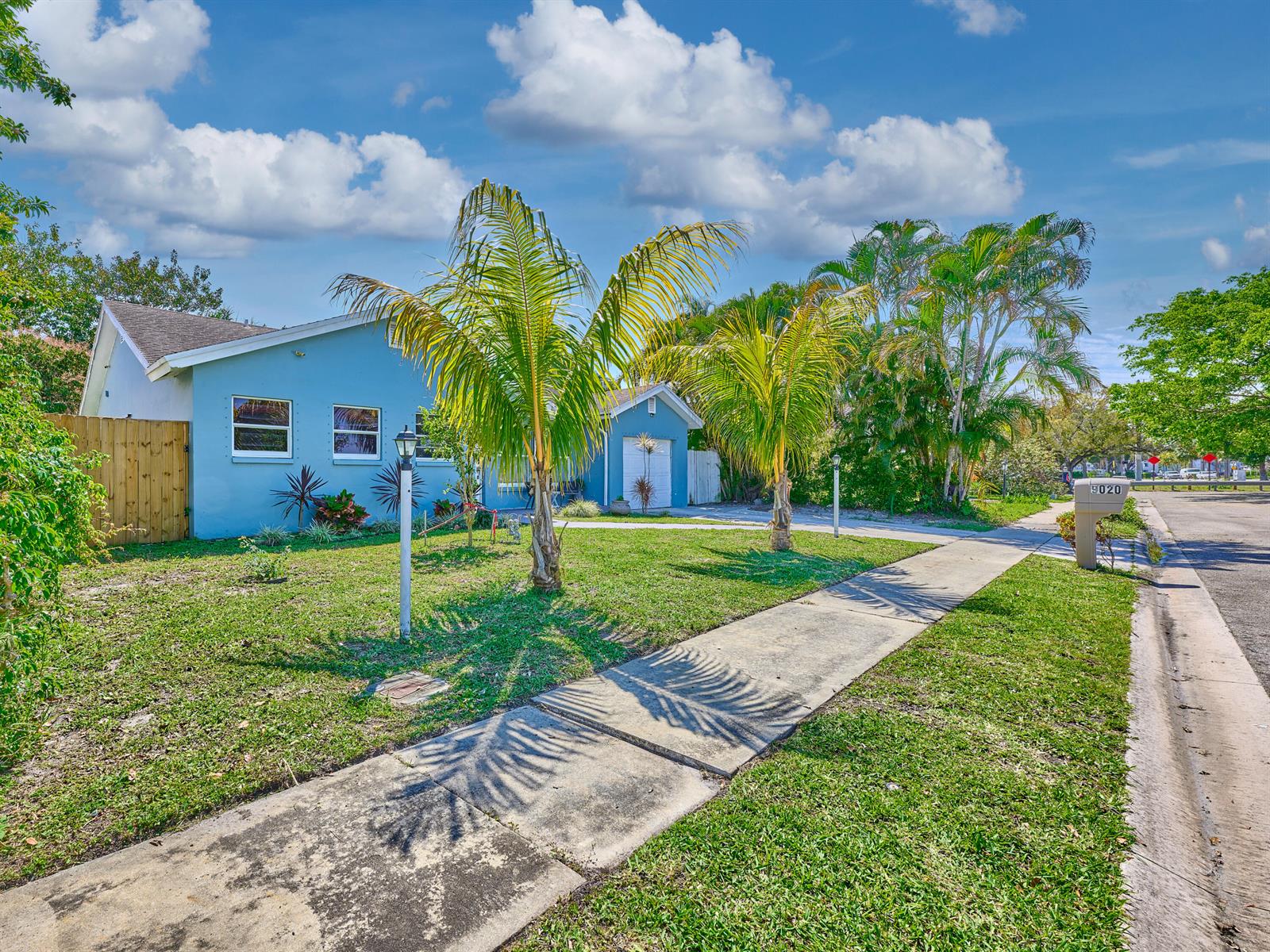 A blue house with a palm-lined front yard and a sidewalk sits under a cloudy sky — 9020 SW 8th Street, Boca Raton FL 33433, BOCA RATON, FL
