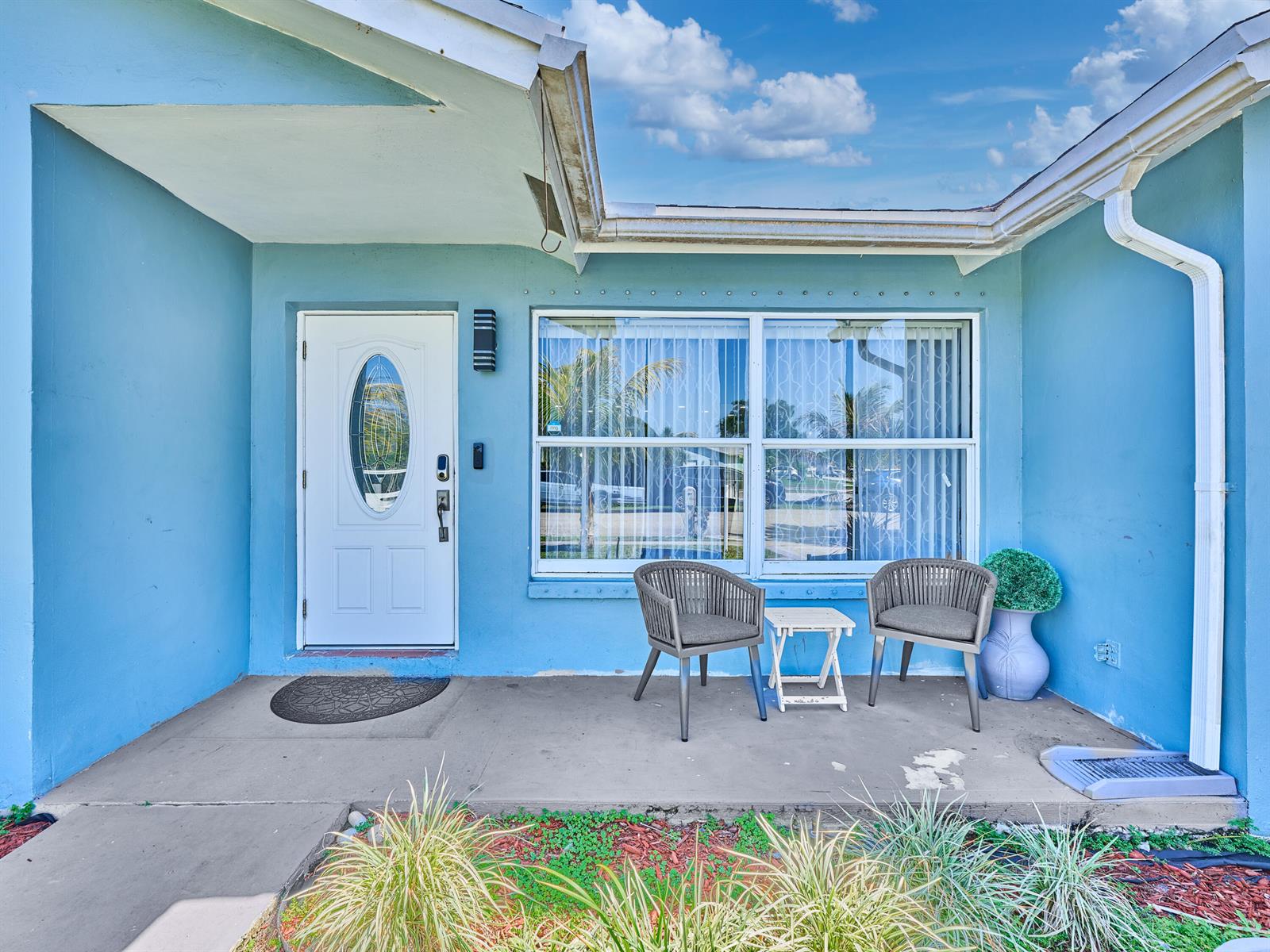 A blue house exterior features a white front door, a large window, and two chairs — 9020 SW 8th Street, Boca Raton FL 33433, BOCA RATON, FL
