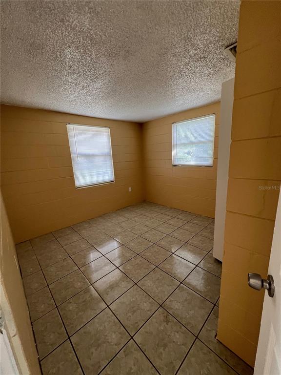 A room with yellow painted block walls, tiled flooring, and two windows with blinds — 3007 14TH ST E, BRADENTON, FL