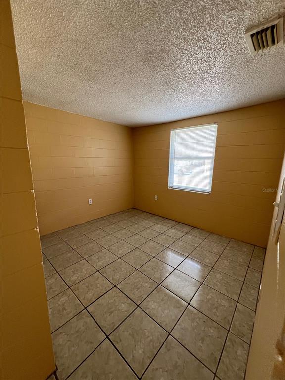 An empty room with yellow painted block walls, tiled flooring, and a single window — 3007 14TH ST E, BRADENTON, FL
