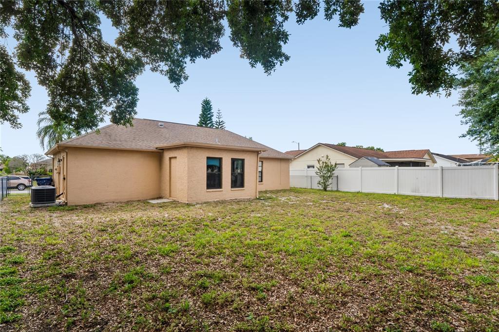 The backyard of a tan house features a grassy lawn and a white vinyl fence — 1238 FUCHSIA DRIVE, HOLIDAY, FL