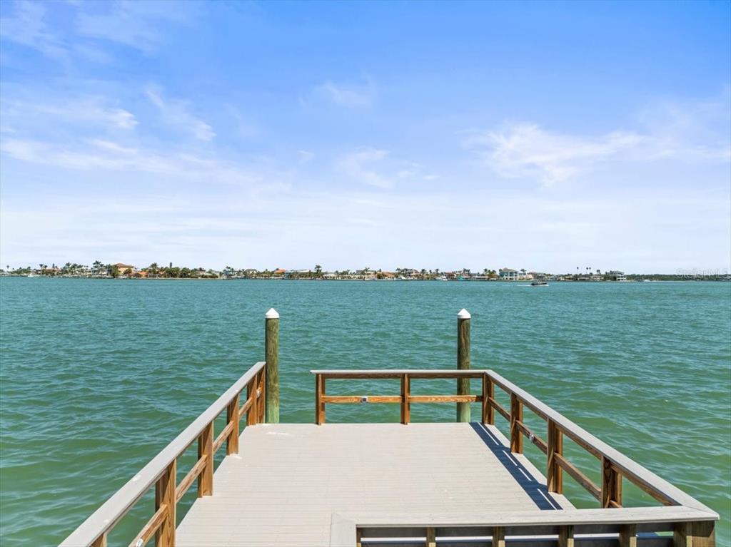 A wooden dock extends over calm water toward a distant shoreline under a blue sky — 6 PARADISE LANE, TREASURE ISLAND, FL