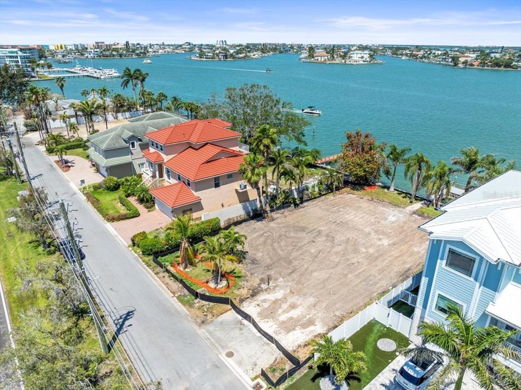 An aerial view shows a vacant waterfront lot situated between two houses along a coastal road — 6 PARADISE LANE, TREASURE ISLAND, FL