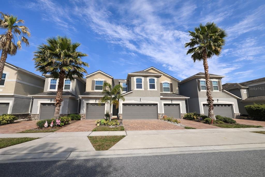 A row of multi-story townhomes with gray stucco facades, attached garages, and palm trees — 3749 BRIGHTON PARK CIRCLE, ORLANDO, FL