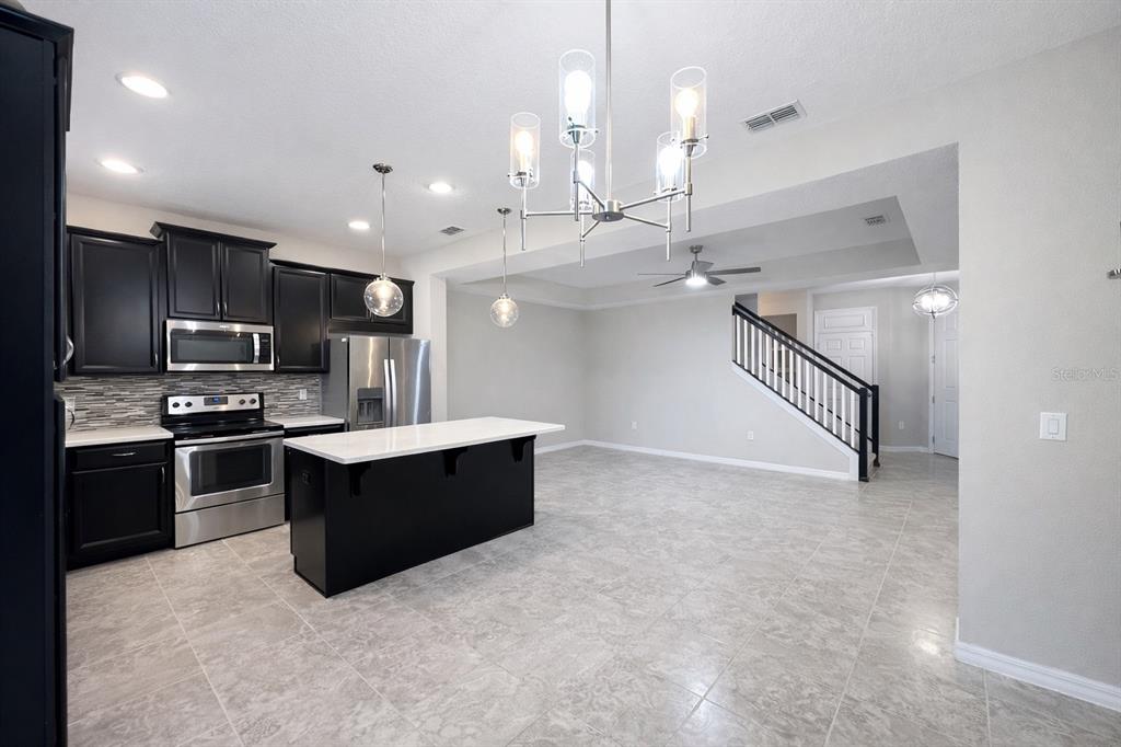 A kitchen with black cabinets, a white island, and tile flooring opens to a staircase — 3749 BRIGHTON PARK CIRCLE, ORLANDO, FL