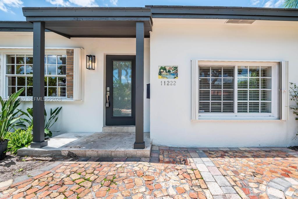 The exterior of a white house features a dark-framed front door and a brick patio — 11222 NE 9th Ave, Biscayne Park FL 33161, BISCAYNE PARK, FL
