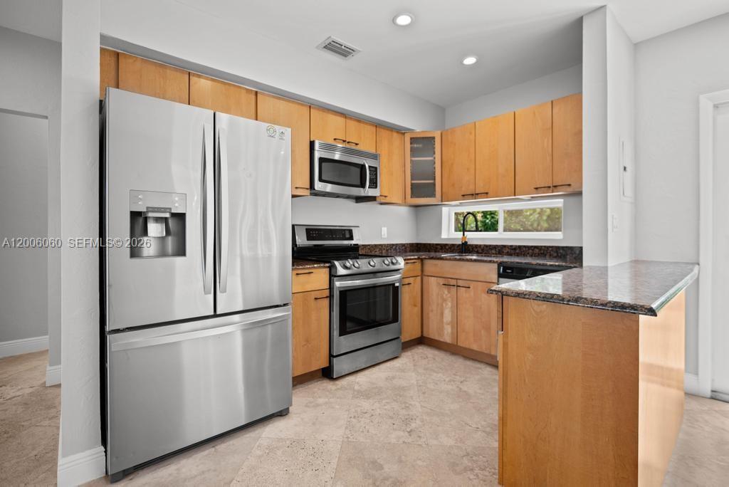 A kitchen features stainless steel appliances, wood cabinets, and granite countertops over tile flooring — 11222 NE 9th Ave, Biscayne Park FL 33161, BISCAYNE PARK, FL
