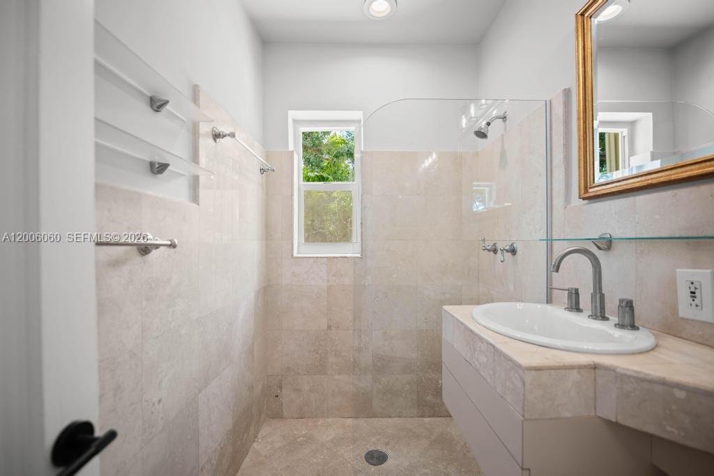 A bathroom features a walk-in shower with beige tile, a vanity sink, and a window — 11222 NE 9th Ave, Biscayne Park FL 33161, BISCAYNE PARK, FL