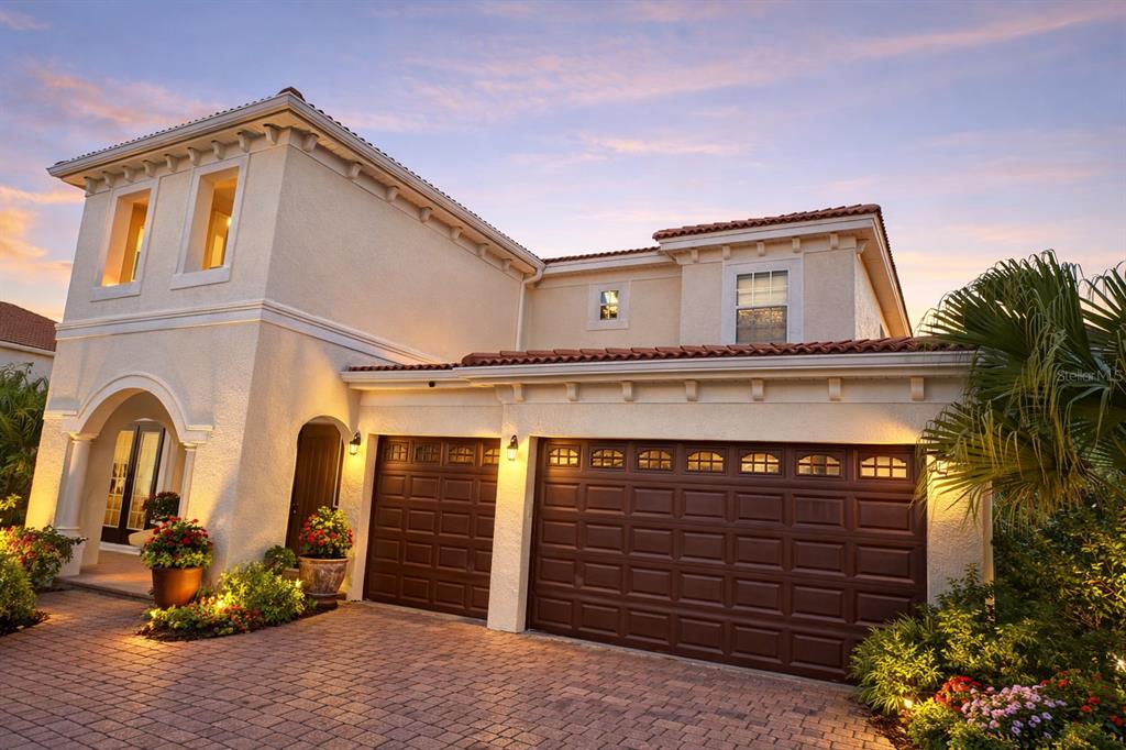 A two-story stucco house with a three-car garage and a brick paver driveway at dusk — 2802 QUIET WATER TRAIL, KISSIMMEE, FL