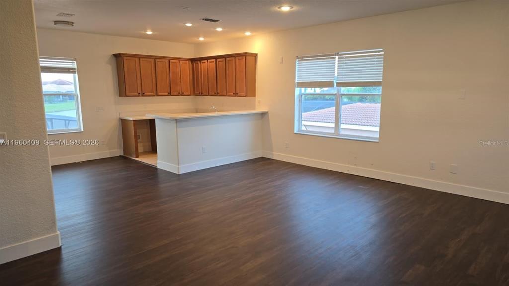 An open-concept room features dark wood flooring, a kitchen with wooden cabinets, and white walls — 2802 QUIET WATER TRAIL, KISSIMMEE, FL