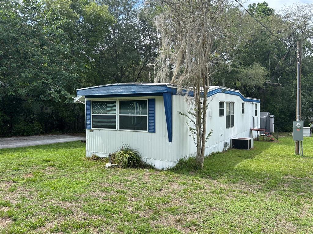 A single-wide mobile home with white siding and blue trim sits on a grassy lot — 10945 SE 132ND PLACE, OCKLAWAHA, FL
