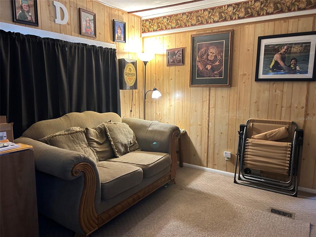 A living room features wood-paneled walls, a tan sofa, and a folding chair — 10945 SE 132ND PLACE, OCKLAWAHA, FL