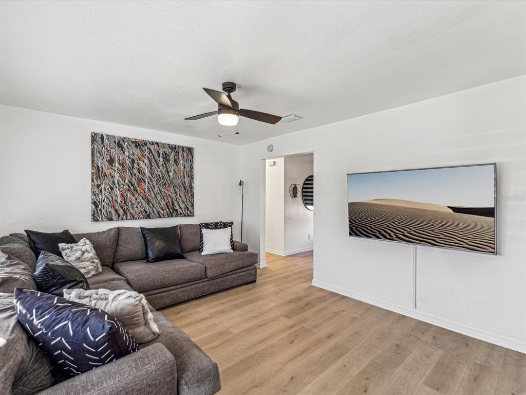 A living room features a grey sectional sofa, wall-mounted television, and light wood flooring — 2000 57TH STREET N, ST PETERSBURG, FL